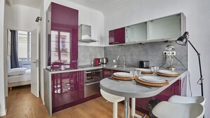 A modern kitchen with a dining area, featuring a grey countertop, red cabinets, and a small dining table with stools. - Apartment Center of Paris (Paris)