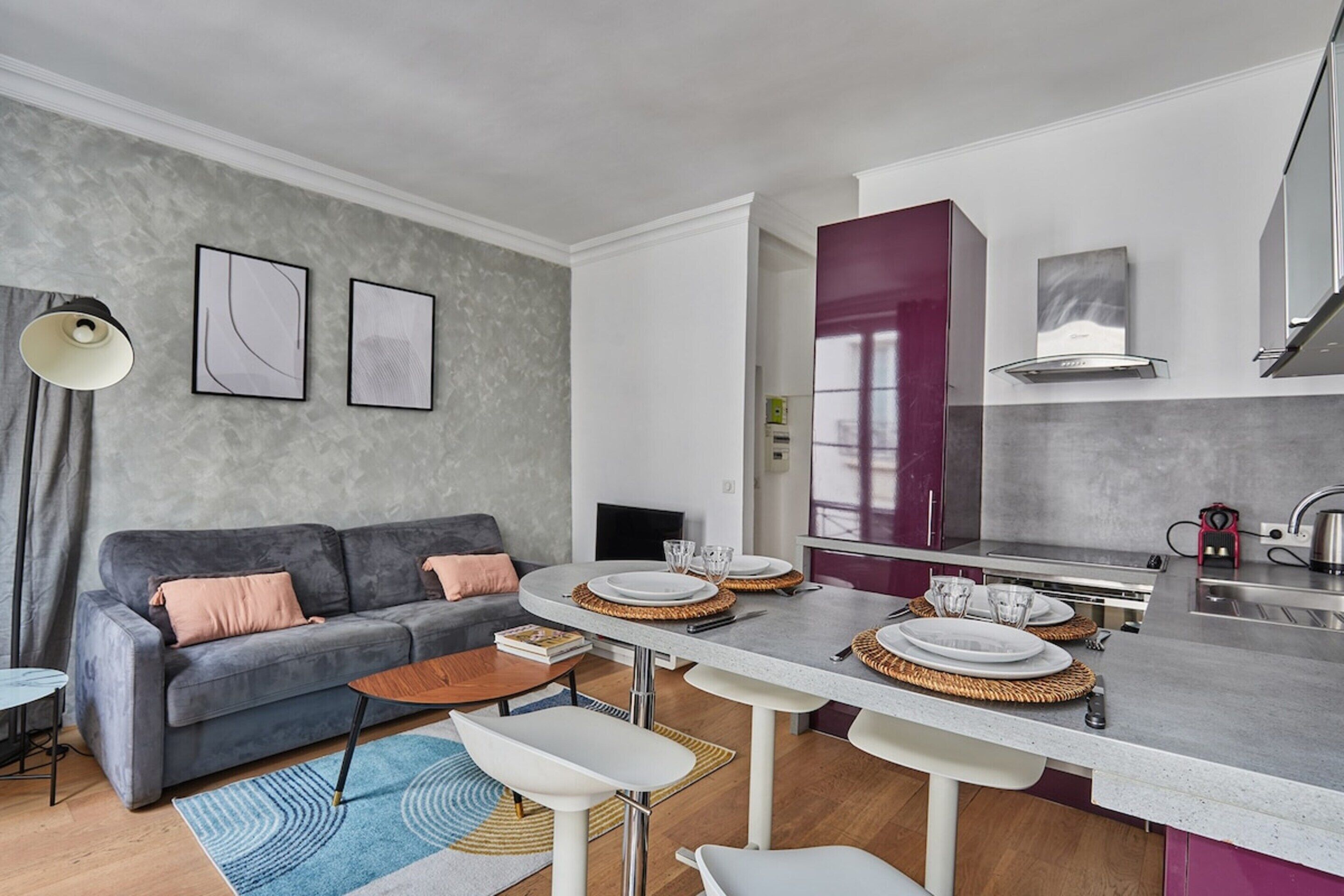 A modern living room with a grey sofa, a coffee table, and a dining area with a kitchen in the background.
