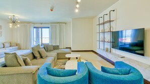Un salon moderne avec un canapé d’angle, un fauteuil bleu, un téléviseur à écran plat et un mur décoratif en marbre.