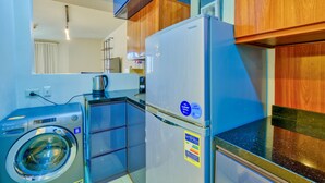 Une cuisine compacte équipée d’un lave-linge, d’un réfrigérateur et de meubles de rangement en bois.