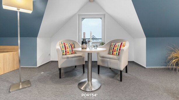 A cozy room with a round table and two chairs, a floor lamp, and a window with a view. - Bude 3 directly on the dike in Dagebüll for 2 persons with water view (Dagebüll)