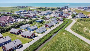 A coastal residential area with houses, a narrow waterway, and a distant view of the sea. - Bude 3 directly on the dike in Dagebüll for 2 persons with water view (Dagebüll)