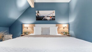 A bedroom with a large bed, a headboard with two wall-mounted lamps, and a framed picture above the bed. - Bude 3 directly on the dike in Dagebüll for 2 persons with water view (Dagebüll)