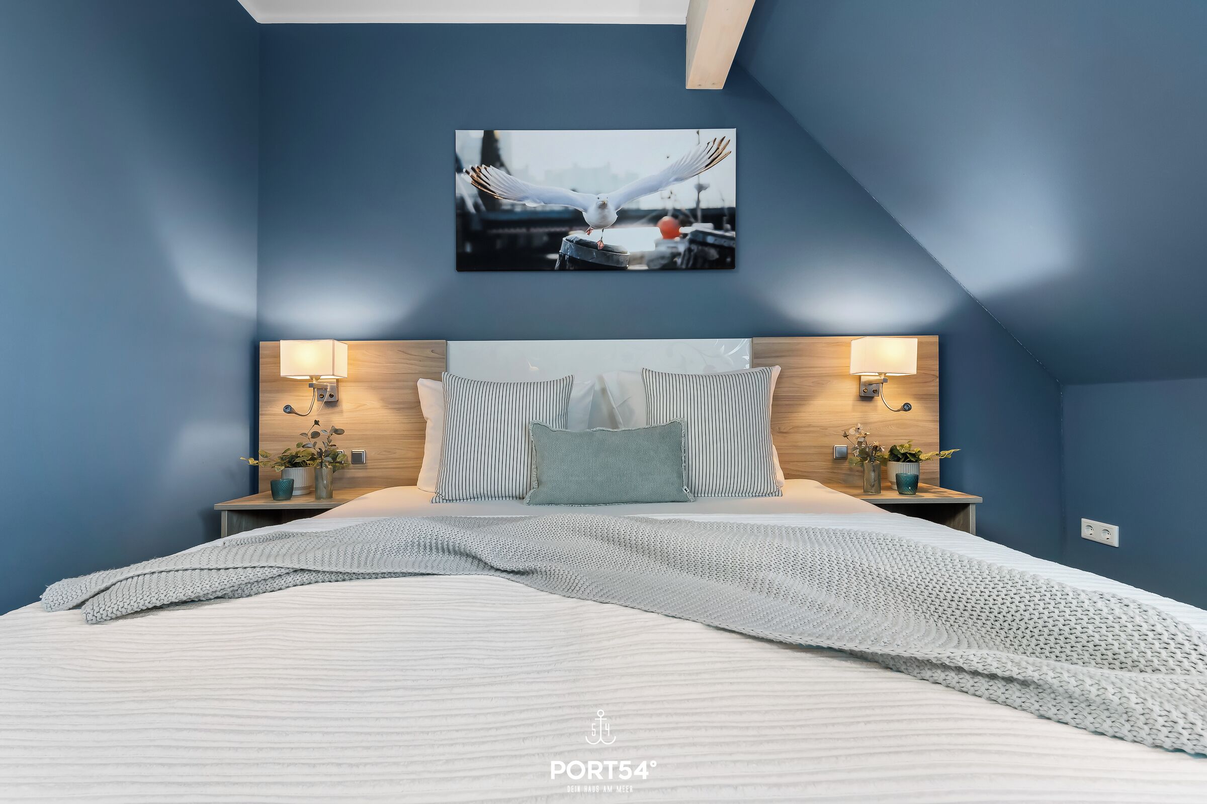 A bedroom with a large bed, two bedside tables with lamps, a wall-mounted picture, and a sloped ceiling.