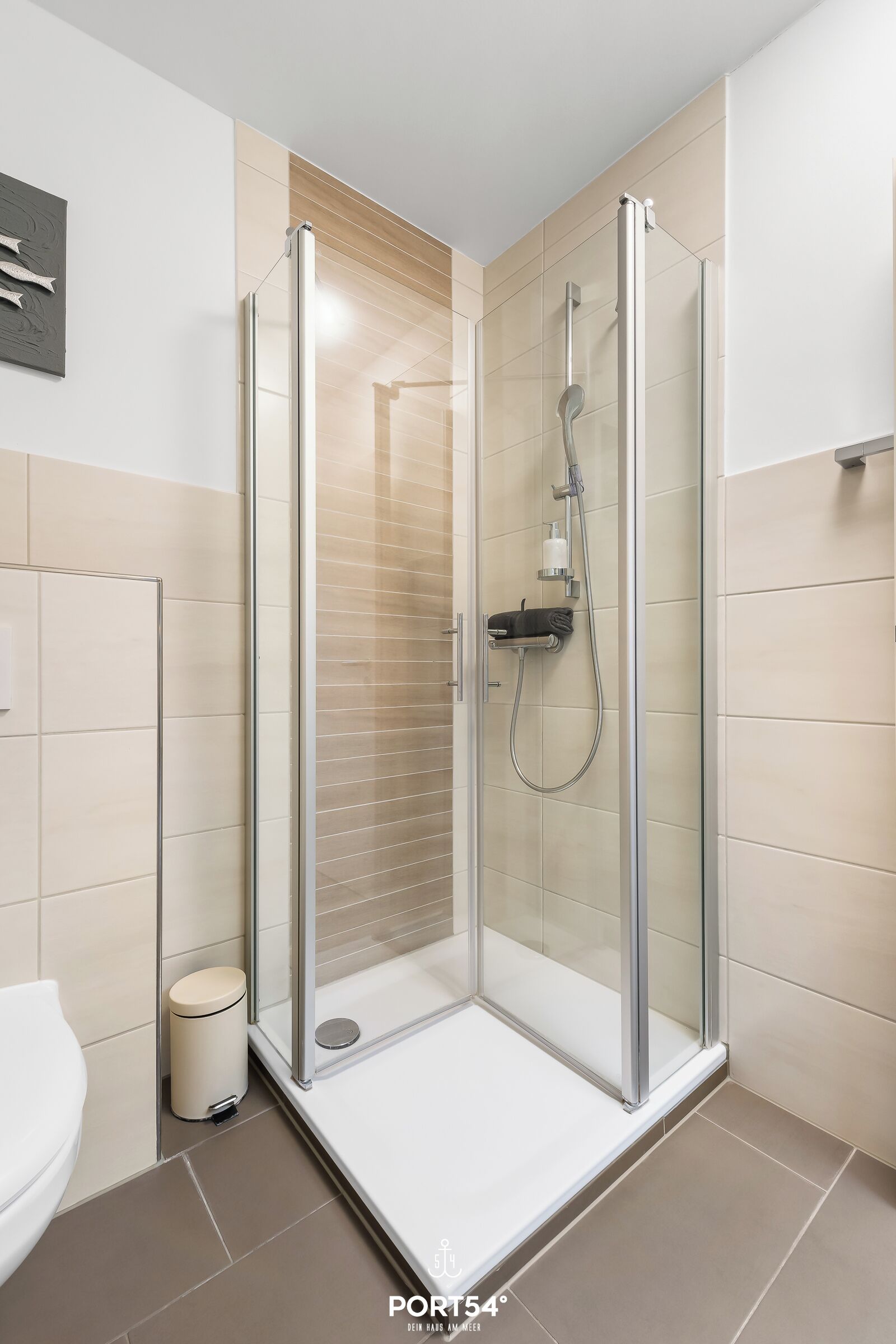 Une salle de bain moderne avec une douche à parois de verre, des toilettes et une poubelle.