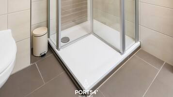 Une salle de bain moderne avec une douche à parois de verre, des toilettes et une poubelle.