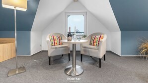 A cozy room with a round table and two chairs, a floor lamp, and a window with a view. - Bude 10 directly on the dike in Dagebüll for 2 persons (Dagebüll)