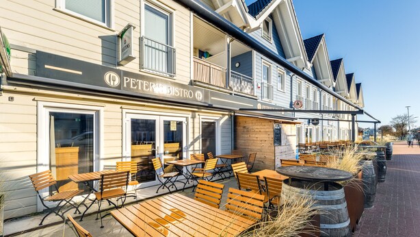 An outdoor seating area with wooden tables and benches at a restaurant named 'PETER'S RESTRO'. - Bude 10 directly on the dike in Dagebüll for 2 persons (Dagebüll)