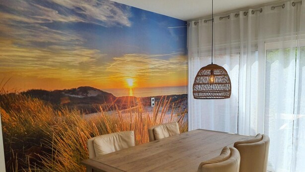 Un coin repas avec une table et des chaises en bois, une fresque murale représentant un coucher de soleil et un luminaire suspendu.