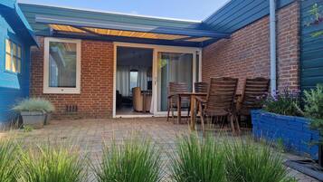 A patio with a brick wall, a blue door, and a covered seating area with wooden chairs.