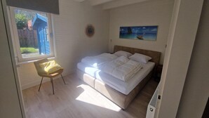 Une chambre à coucher avec un lit, une chaise, un tableau accroché au mur et une fenêtre donnant sur l’extérieur.