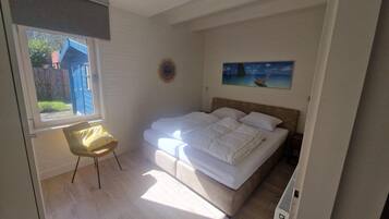 A bedroom with a bed, a chair, a painting on the wall, and a window with a view of the outside.