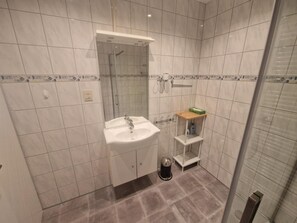 Un bagno con lavandino, specchio, doccia e un piccolo ripiano con articoli da toilette.