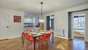 A dining area with a wooden herringbone floor, a table set for four with orange chairs, and a pendant light above. - Superb 3 Bedroom Flat in the Center of Paris (Paris)