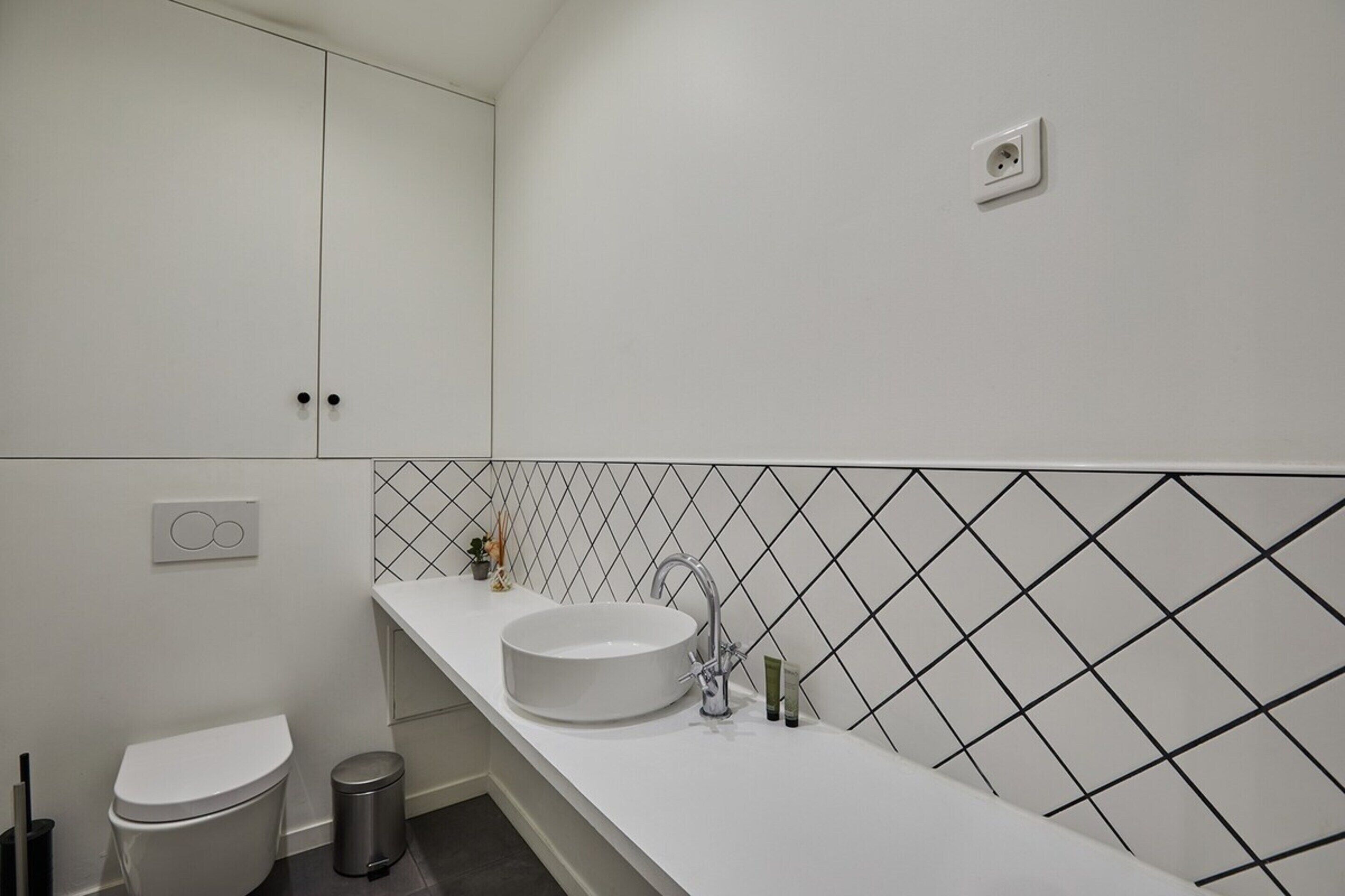 Une salle de bain moderne avec un lavabo blanc, des toilettes et une poubelle.