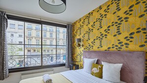 A hotel room with a large window, a bed with a striped bedspread, and a patterned yellow wall. - Superb 3 Bedroom Flat in the Center of Paris (Paris)