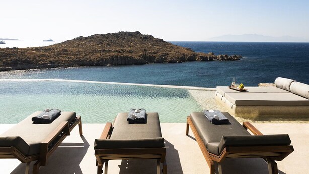 Zona de descanso junto a la piscina con tumbonas y vistas al mar y una isla rocosa.