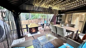 Een terras buiten met rieten meubels, een tafel met glazen blad en een vuurkuil.