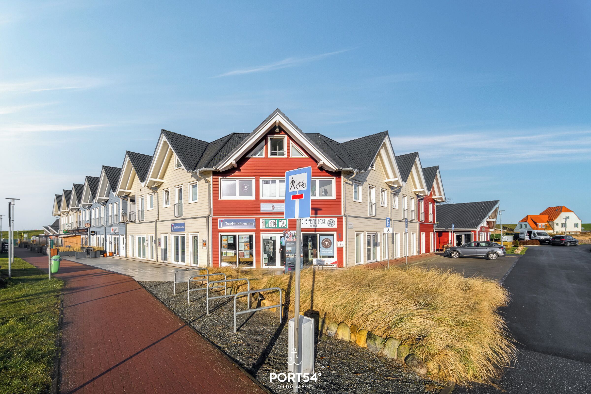 A row of modern houses with a red and white facade, a bike-sharing station, and a clear sky.