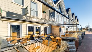 An outdoor seating area with wooden tables and benches at a restaurant named 'PETER'S RESTRO'. - Bude 8 directly on the dike in Dagebüll for 2 persons with water view (Dagebüll)