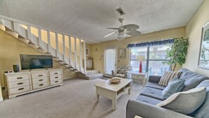 A living room with a staircase, a ceiling fan, a sofa, a coffee table, and a television. - Villa Chateau! Steps to the Beach! (Panama City Beach)