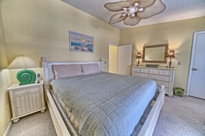 A bedroom with a bed, nightstand, dresser, and a ceiling fan. - Villa Chateau! Steps to the Beach! (Panama City Beach)