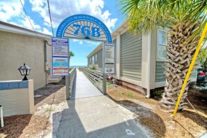 Un chemin menant à une maison de plage, avec un panneau indiquant l’absence de sauveteur et les règles à respecter sur la plage.