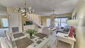 A spacious living room with a glass dining table, white sofas, and a staircase leading to another level. - Villa Chateau! Steps to the Beach! (Panama City Beach)
