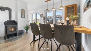 A modern kitchen with a built-in fireplace, a dining area with a wooden table and chairs, and large windows offering a view of the outside. - Vacation apartment Küstenhuus in the North Sea resort: A vacation at the North Sea with sauna, (Büsum)