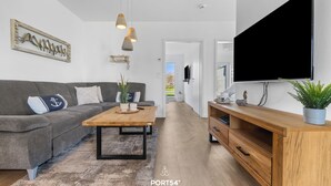 A modern living room with a grey sofa, wooden coffee table, and a large TV mounted on the wall. - Vacation apartment Küstenhuus in the North Sea resort: A vacation at the North Sea with sauna, (Büsum)