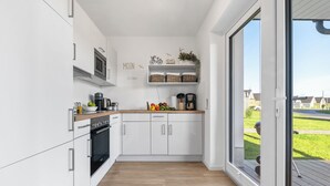 A modern kitchen with white cabinetry, a wooden countertop, and a view through a glass door to an outdoor area. - Vacation apartment Küstenhuus in the North Sea resort: A vacation at the North Sea with sauna, (Büsum)