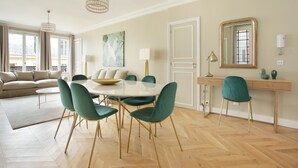 A modern living room with a round dining table, teal chairs, a beige sofa, and a large window with curtains. - Sublime Apartment Haussmann Opera (Paris)