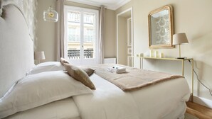 A neatly made bed with a fluffy blanket, a bedside lamp, and a window with a view of buildings. - Sublime Apartment Haussmann Opera (Paris)