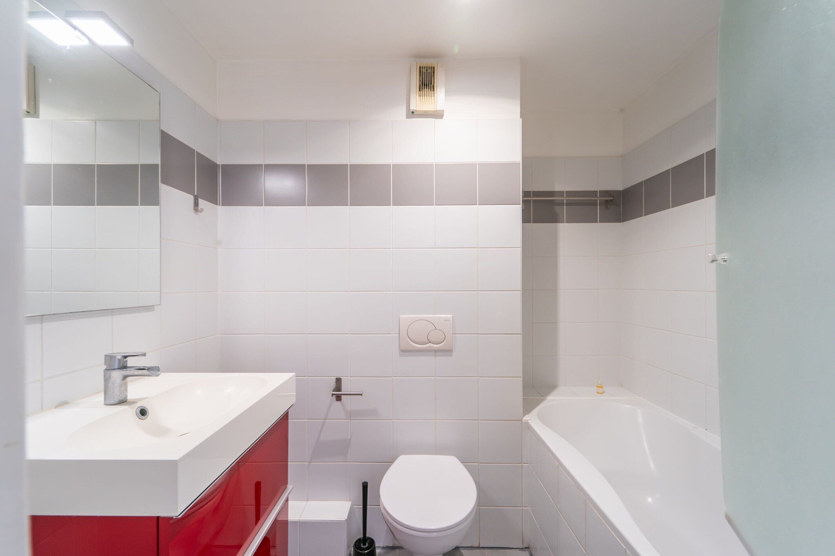 A bathroom with a white sink, red cabinet, white toilet, and a white bathtub.