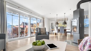 En moderne stue med et stort glasdør, der fører ud til en balkon, et spiseområde med bord og stole, og et køkken med indbygget komfur.