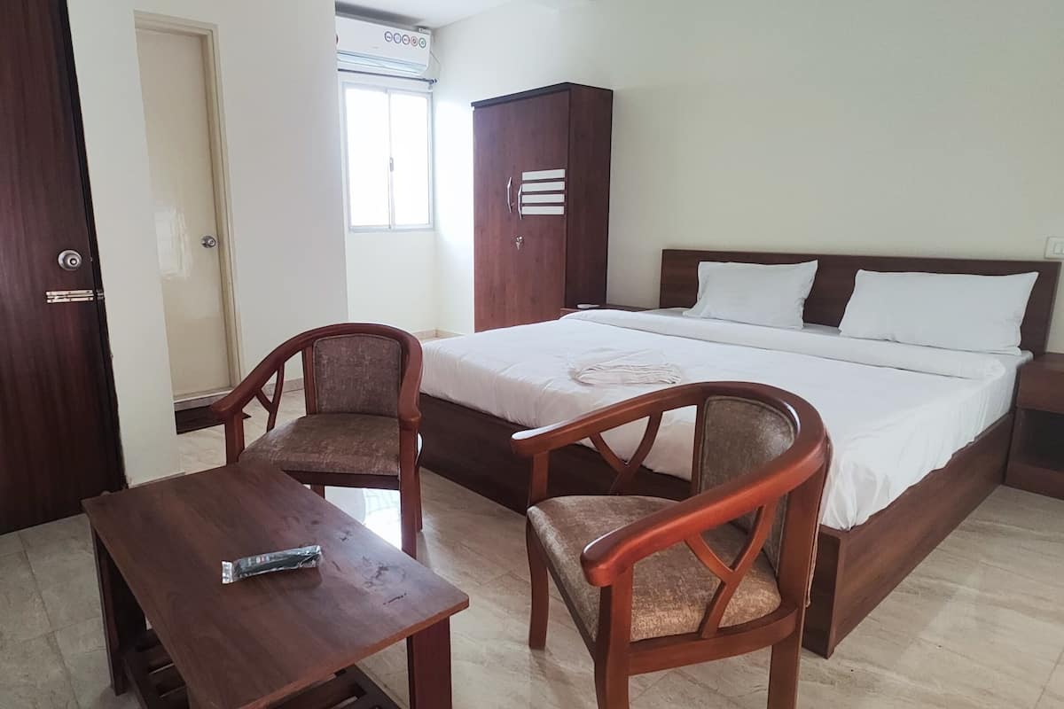 A bedroom with a bed, two wooden chairs, a small table, a wardrobe, and a nightstand.