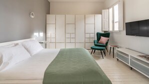 Una habitación de hotel moderna con una cama grande, una silla verde, una mesita pequeña, un televisor y un armario corredero.