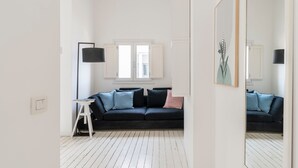 Una sala de estar moderna con un sofá de color oscuro, un taburete blanco pequeño y una lámpara de pie.