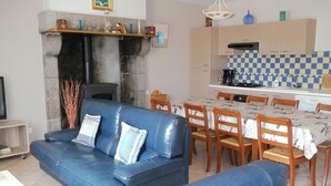 Una sala de estar con un sofá azul, chimenea y una zona de cocina con salpicadero a cuadros.