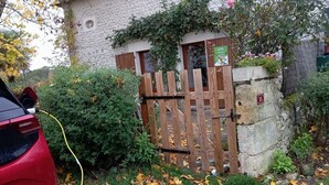 A gated entrance with a wooden gate, a car parked outside, and a building with a stone wall and ivy. - Cottage Le Breuil in Périgord - Charm and Comfort (Salles-Lavalette)