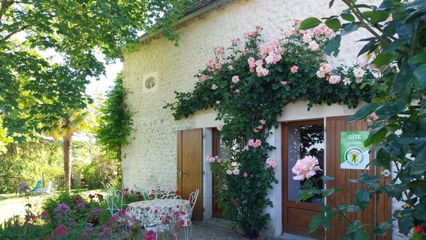A rustic building with a garden entrance, a table with a fruit-patterned tablecloth, and a sign indicating a Gîte. - Cottage Le Breuil in Périgord - Charm and Comfort (Salles-Lavalette)