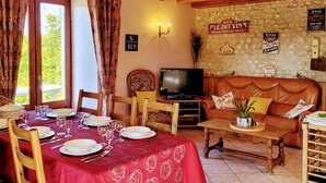 A cozy dining area with a red tablecloth, wooden chairs, and a television in the background. - Cottage Le Breuil in Périgord - Charm and Comfort (Salles-Lavalette)