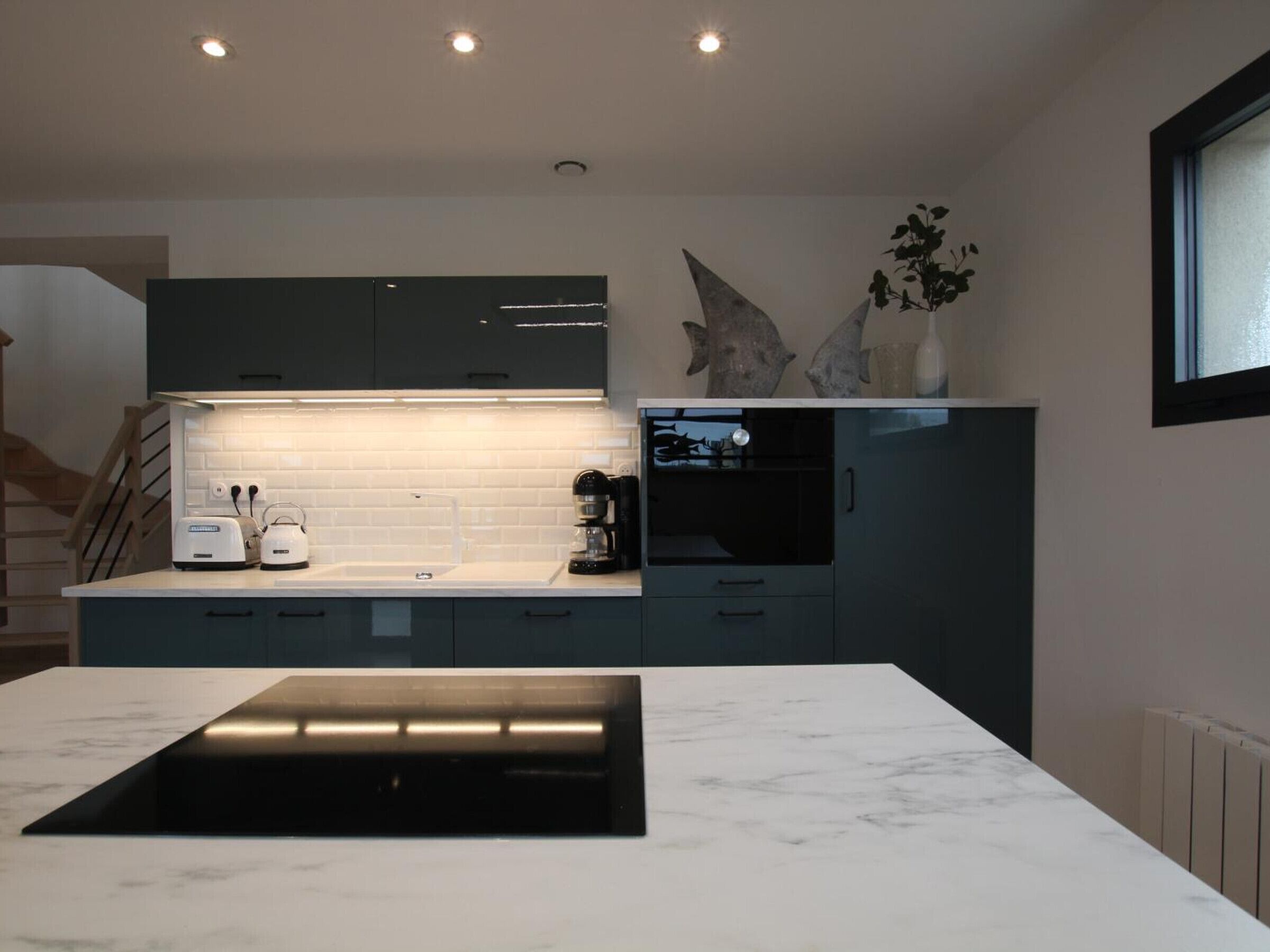 Une cuisine moderne dotée d’un plan de travail en marbre, de meubles de rangement aux couleurs sombres et d’un four encastré.