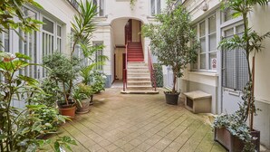 A narrow courtyard with a central staircase, surrounded by potted plants and a tiled floor. - Charming Apartment Center of Paris (Paris)