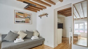 A modern living room with a grey sofa, wooden beams, a framed abstract painting, and a wooden shelf with candles. - Charming Apartment Center of Paris (Paris)