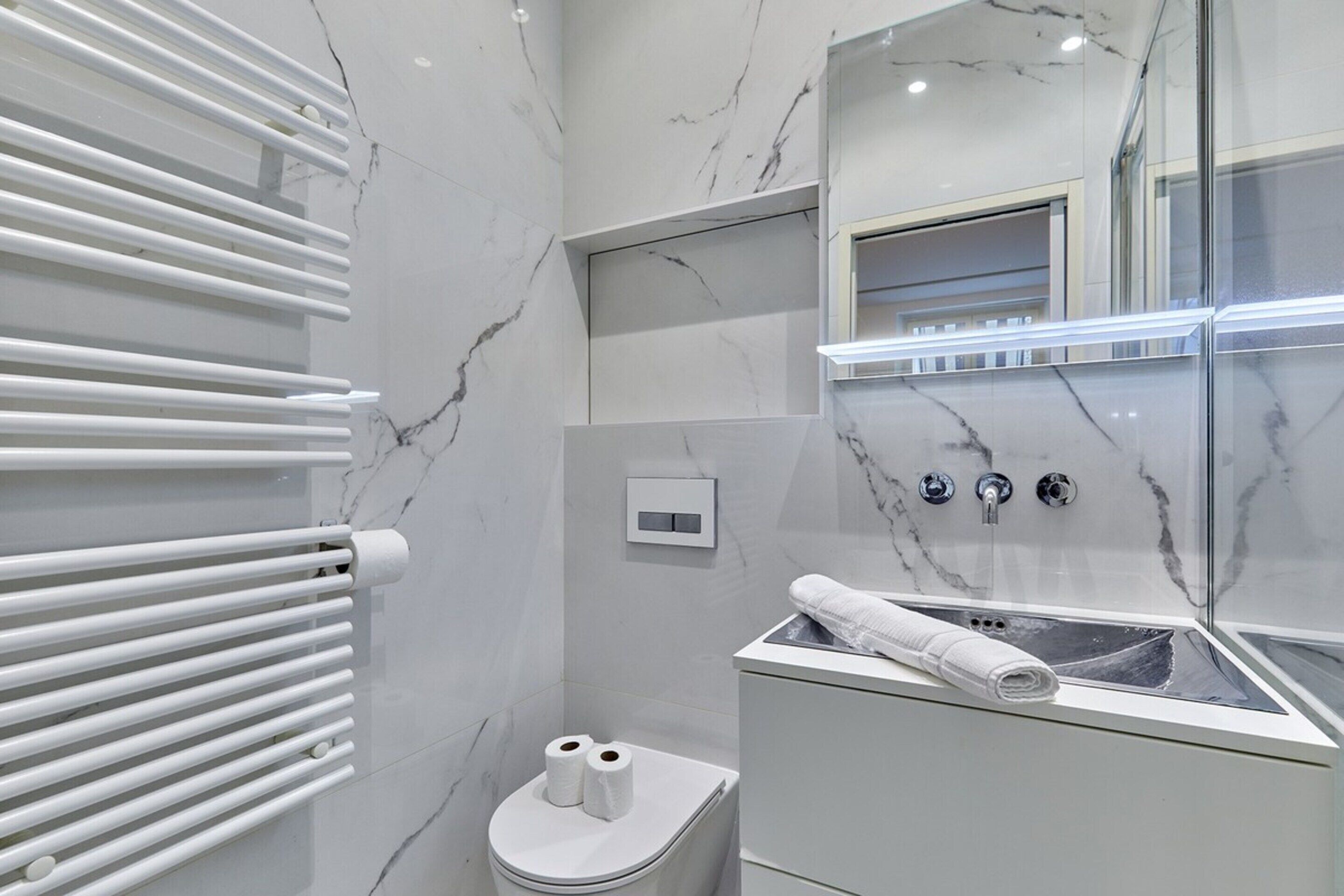 Um banheiro moderno com parede de mármore branco, box de vidro, vaso sanitário branco e porta-toalhas.