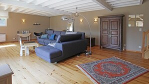 A spacious living area with a large grey sofa, a wooden floor, a patterned rug, and a wooden cabinet. - Spacious house near the beach, perfect for families, pets allowed (Saint-Germain-sur-Ay)