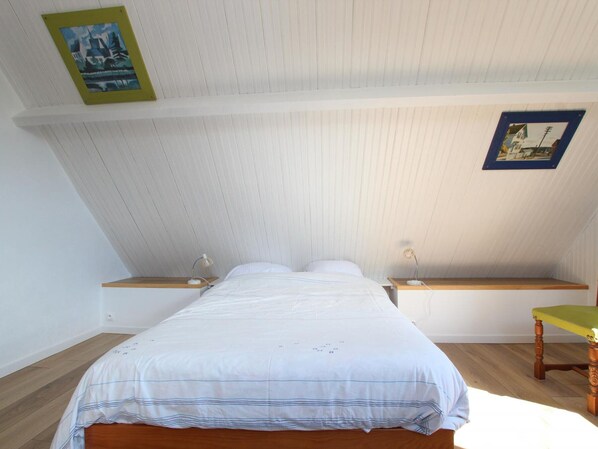 A bedroom with a bed, two bedside tables, a wooden bench, and two framed pictures on the wall.