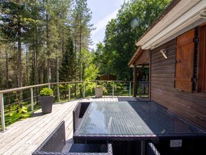 A wooden deck with a glass table and chairs, surrounded by trees. - Rustic chalet in the heart of Black Périgord with terrace & all comforts included (Saint-Pompont)