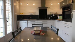 Una cocina moderna con armarios blancos, encimera negra y campana extractora de acero inoxidable. Hay una mesa de comedor con sillas y un jarrón con flores amarillas.